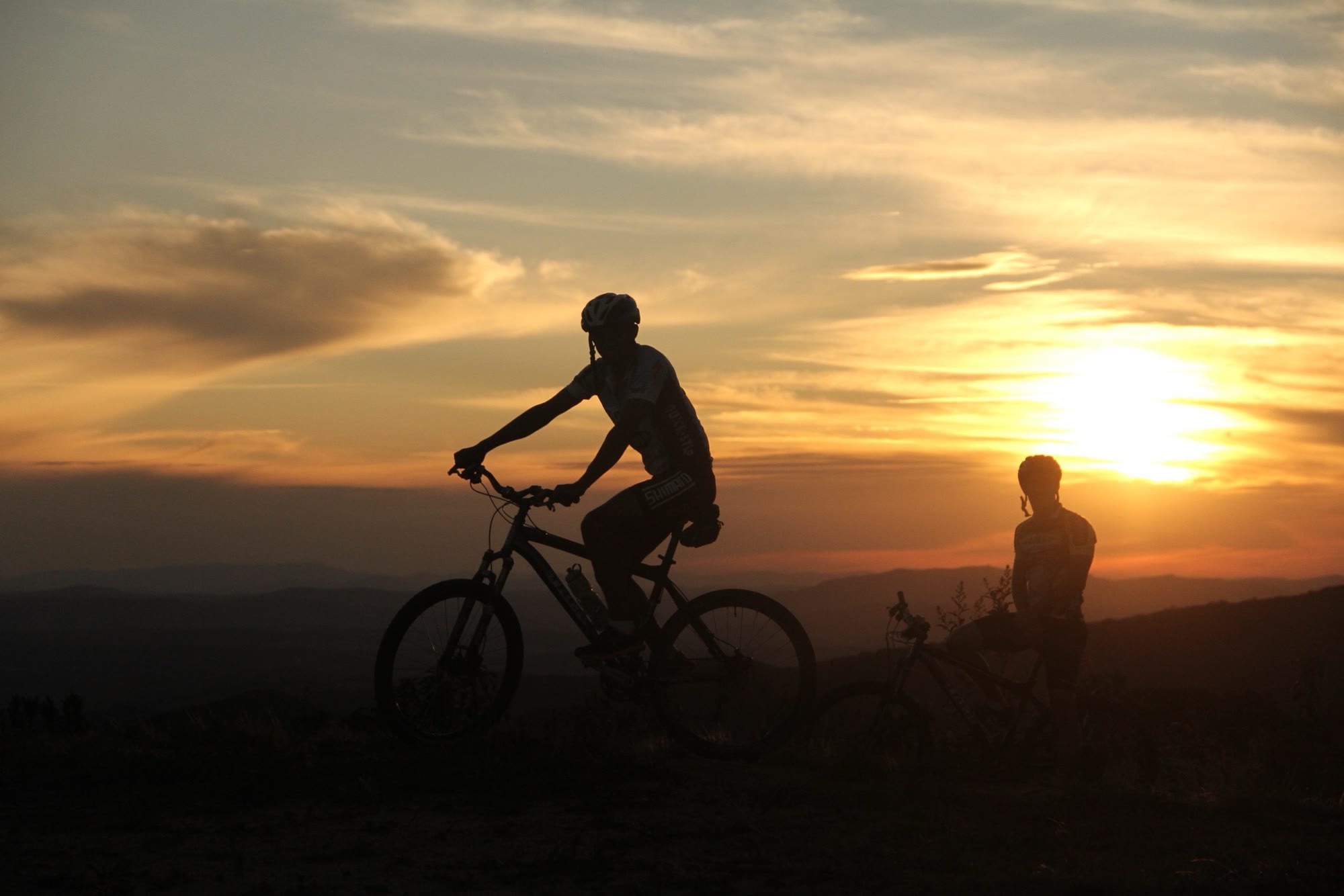 Dois ciclistas em silhueta no alto do território, ao pôr do sol